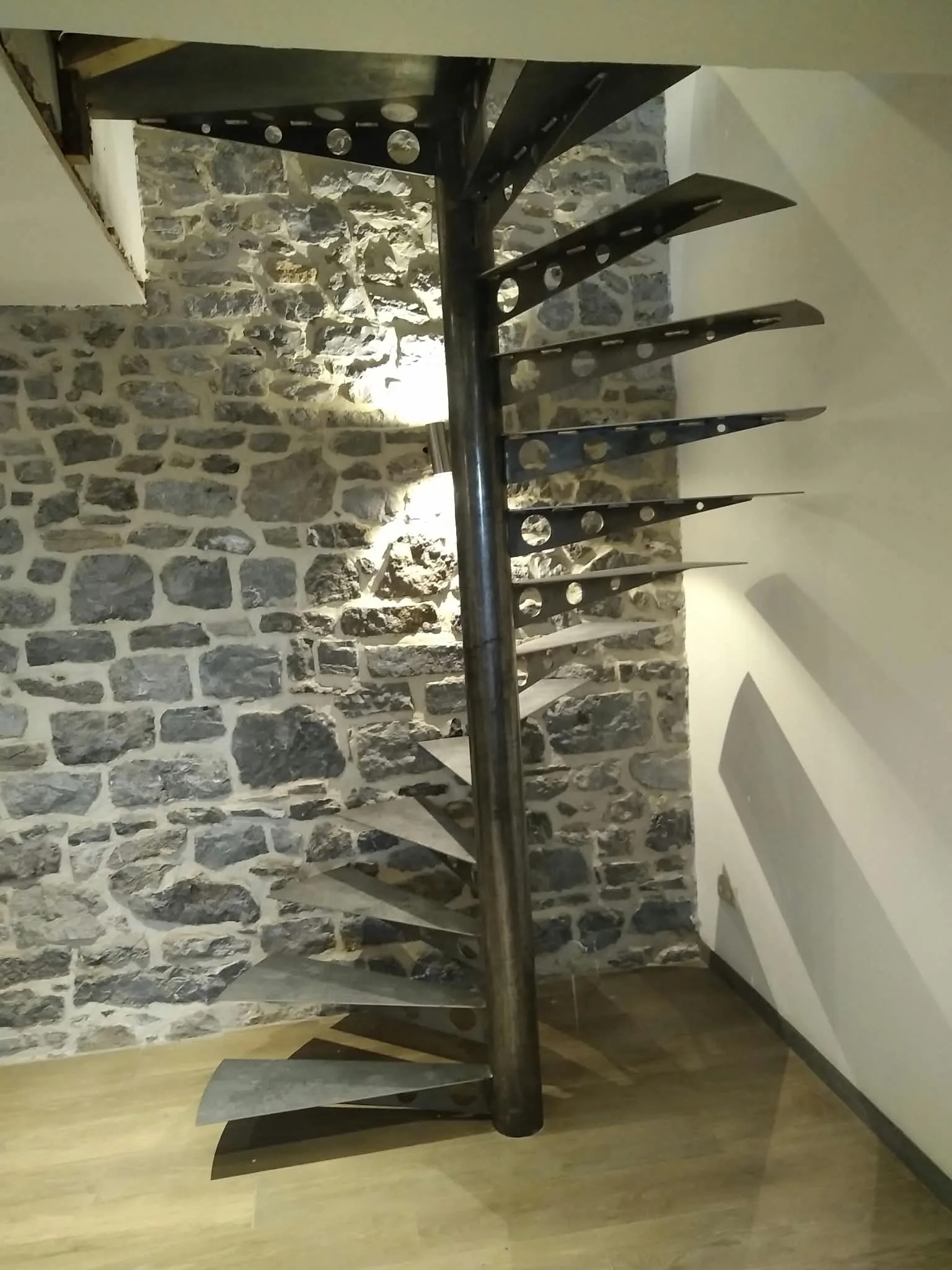 Escalier hélicoïdal métallique sur mesure devant un mur en pierre