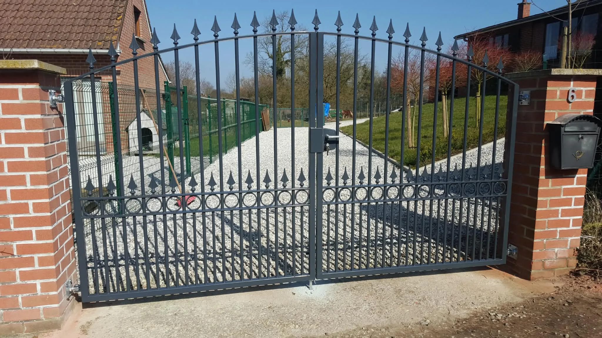Portail battant ornemental gris motorisé installé entre deux piliers en briques
