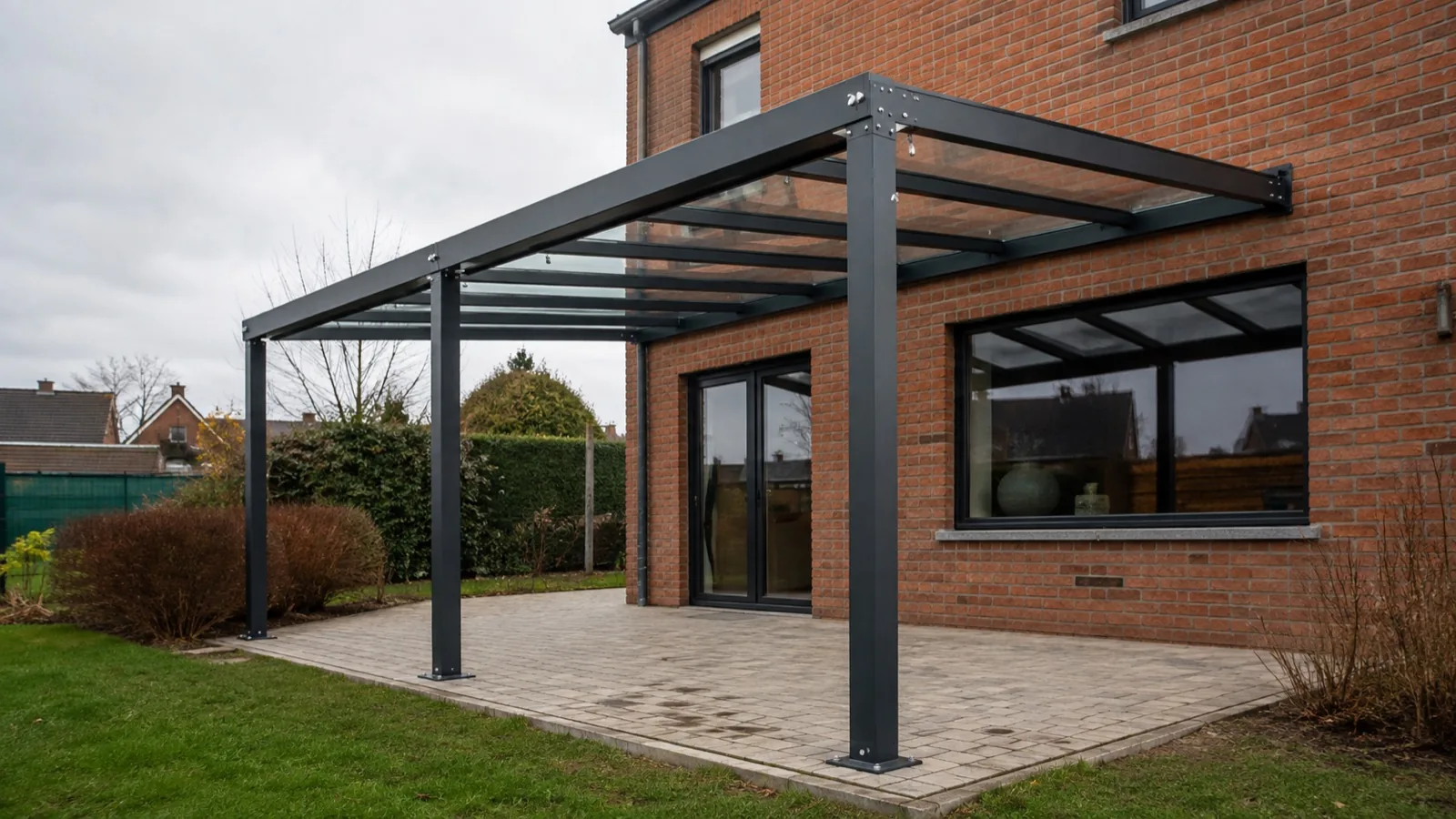 Pergola en structure métallique noire avec toiture vitrée devant une maison